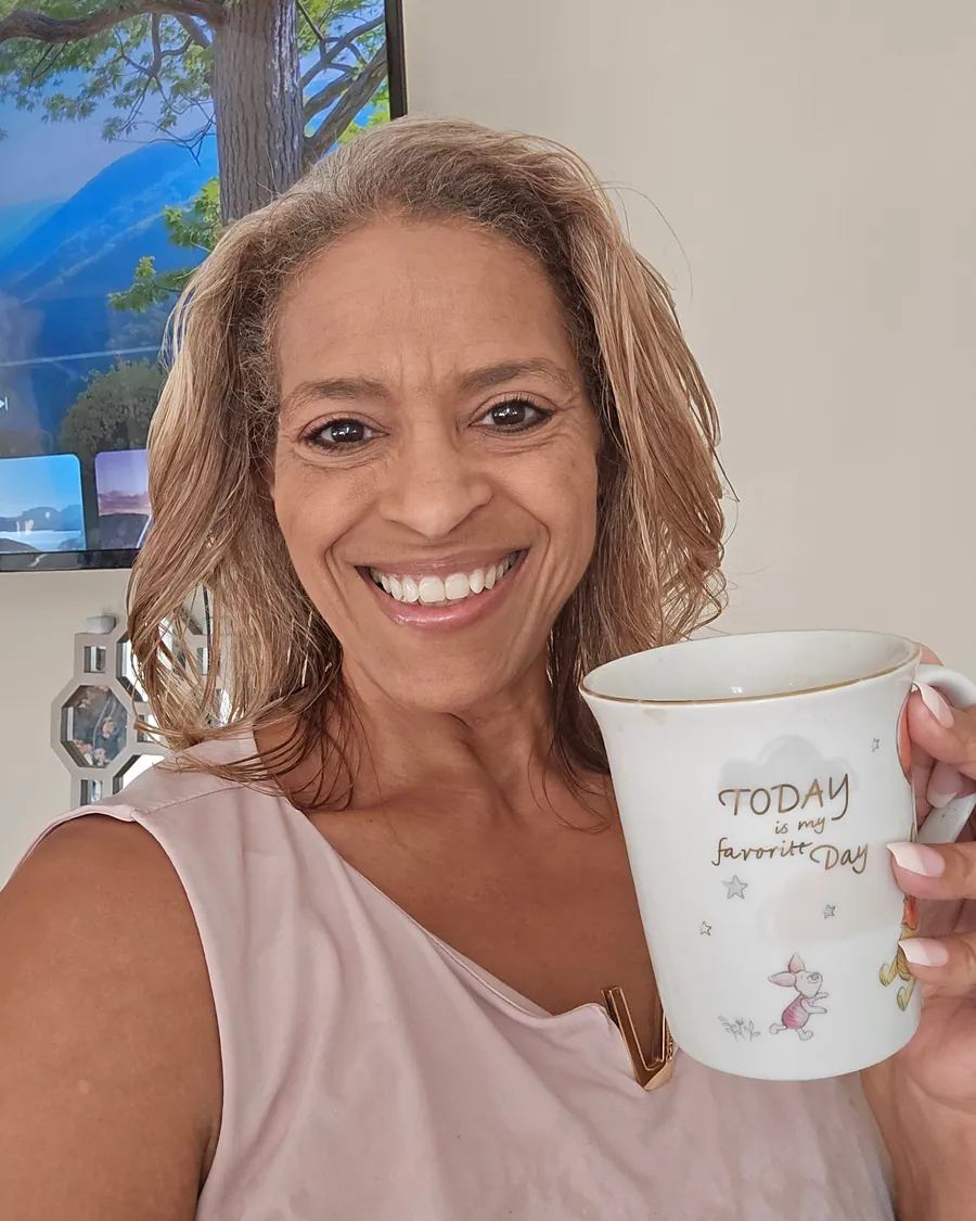 Amy J. Watson smiling at home, holding a mug that reads “Today is my favorite day.”